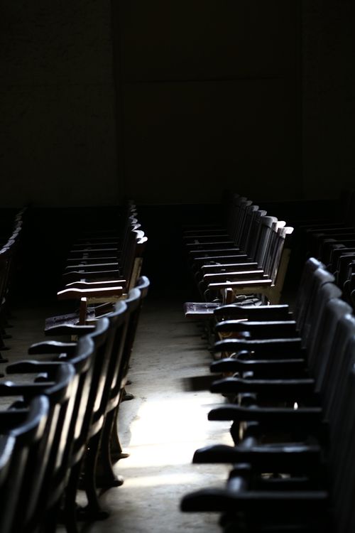 昏暗礼堂中的空椅，象征缺席者、历史记忆与见证责任
